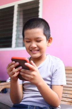 Neşeli bir çocuk dışarıda oturur ve akıllı telefonuyla mutlu bir şekilde iletişim kurar. Onun parlak gülümsemesi teknolojinin ve gençliğin neşeli ruhunu sergiliyor..