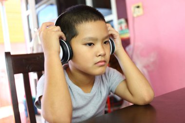 Genç bir çocuk bir masada oturuyor, kulaklık takıyor, derinden müzik dinlemekle meşgul. Onun odaklanmış ifadesi ev ortamında sesin neşesini yakalar..