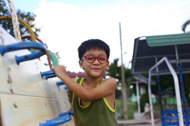 Gözlüklü neşeli bir çocuk açık hava ortamında çocuk parkına tırmanmayı seviyor. Çocukluk ve macera ruhunu somutlaştırıyor..