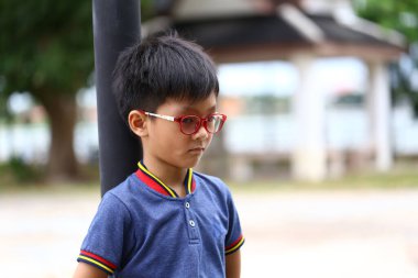 Renkli gözlük takan düşünceli genç bir çocuk dışarıda dikiliyor ve bir anlık tefekkür yansıtıyor. Bu sahne çocukluğun masumiyetini ve merakını yakalar..