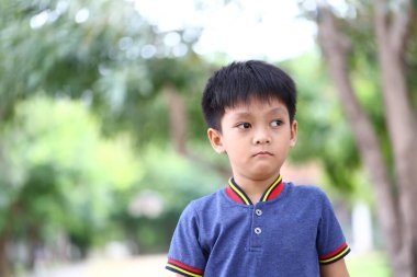 Genç bir çocuk düşünceli bir şekilde çevresi yeşilliklerle çevrili dışarıda duruyor. Günlük kıyafetleri ve düşünceli ifadesi çocukluk masumiyetinin ve merakının özünü yansıtıyor..