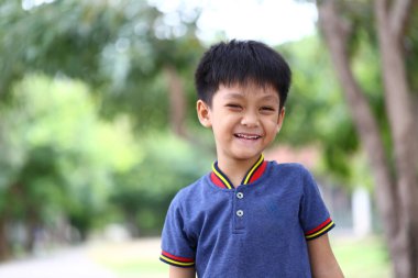 Neşeli genç bir çocuk açık hava ortamında sıcak bir şekilde gülümser. Doğadaki çocukluk mutluluğunun ve kaygısız anların özünü yakalar..