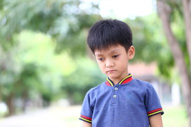 Genç bir çocuk dışarıda duruyor, dalgın bir ifadeyle aşağıya bakıyor. Huzur ortamı ve yumuşak odaklı arka plan onun düşünceli ruh halini güçlendirir..