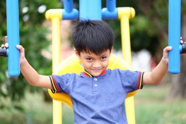 Neşeli genç bir çocuk renkli oyun alanı ekipmanlarıyla oynamayı, güneşli bir açık havada neşe ve kaygısız anlar sergilemeyi sever..