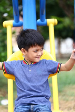 Neşeli genç bir çocuk parktaki renkli bir kaydırağın üzerinde eğleniyor, çocukluk ve açık hava eğlencesi ruhunu sergiliyor..