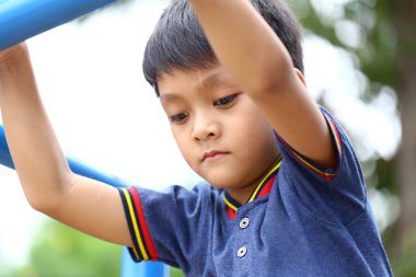Bir çocuk oyun parkında tırmanma çerçevesinde oynarken derinden odaklanmış. İfadesi, açık hava ortamında konsantrasyon ve neşe gösteriyor..