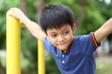 Neşeli bir çocuk, neşeli bir oyun bahçesinde oyun oynamaktan zevk alıyor. Güneşin altında açık hava aktiviteleriyle meşgul olurken mutluluk ve enerji gösterisi yapıyor..