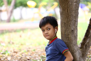 Genç bir çocuk, çocuk parkında bir ağaca yaslanırken, müzikten zevk alır, gençlik ruhunu somutlaştırır ve doğal bir ortamda rahatlatır..