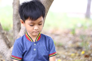 Düşünceli genç bir çocuk dalgın dalgın dalgın bir ağacın altında oturuyor. Bu huzurlu an, doğadaki çocukluğun masumiyetini ve huzurunu yakalar..