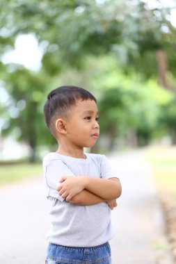 Genç bir çocuk, yeşil yemyeşil, merakla ve masumiyetle dolu sakin bir parkta kollarını kavuşturarak düşünceli bir şekilde duruyor. Herhangi bir çocukluk temalı proje için mükemmel.
