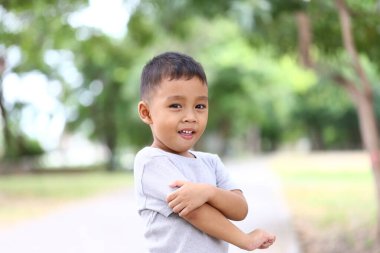 Güneşli bir parkta dururken gülümseyen neşeli bir çocuk. Bu iç açıcı görüntü çocukluğun masumiyetini ve neşesini canlı, doğal bir ortamda yakalar..