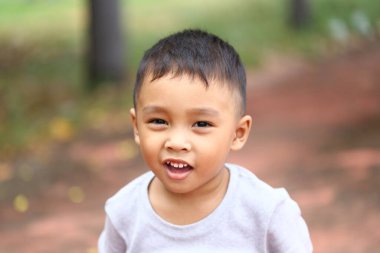 Neşeli genç bir çocuk, açık havada saf mutluluğu gösteren parlak bir şekilde gülümser. Bu portre masumiyet ve çekiciliği yakalar..