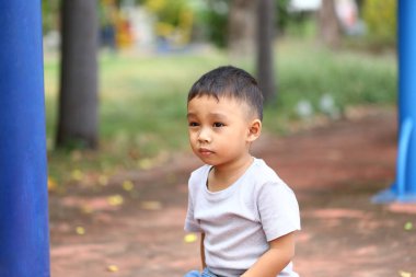 Genç bir çocuk düşünceli bir şekilde parkta oturur ve doğanın içindeki masumiyet ve merakı yakalar. Çocukluk temaları için mükemmel.