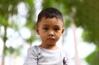 Yeşilliklerle çevrili, ciddi bir ifadeyle dışarıda duran genç bir çocuk. Bu portre masumiyeti ve merakı sakin bir ortamda yakalıyor..