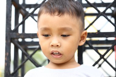 Açık havada genç bir çocuk çocukluğun masumiyetini ve merakını yansıtan düşünceli bir ifade sergiliyor. Bakışları keşif ve meraka işaret ediyor..