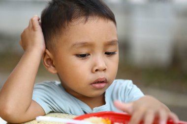 Genç bir çocuk dışarıda oturur, yemeğini bir tabakta incelikle inceler. İfadesi masumiyet ve merakı yakalıyor, aile odaklı temalar için mükemmel..