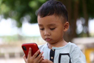 Açık hava ortamında akıllı telefonuna odaklanan genç bir çocuk, doğal ortamda teknolojiyle olan ilgisini ve merakını sergiliyor..