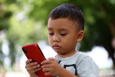 Açık hava ortamında akıllı bir telefona dikkatle bakan küçük bir çocuk masumiyet ve teknolojinin kesiştiği yeri gösteriyor. Sosyal medya temaları için mükemmel.