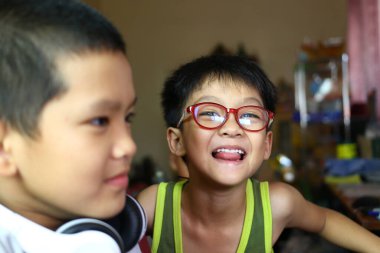 İki neşeli çocuk, biri gözlüklü, diğeri kulaklıklı, kapalı alanda neşeli bir anı paylaşıyor. Onların neşeli ifadeleri çocukluk mutluluğunun ve arkadaşlığın özünü yansıtır..