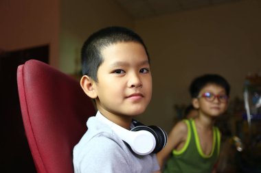 Kapalı bir ortamda otururken kulaklıklı neşeli bir çocuk gülümsüyor. Neşeli tavırları çocukluk ve arkadaşlığın neşesini yansıtıyor..