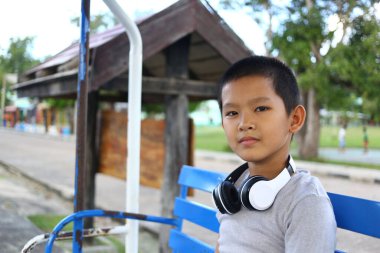 Genç bir çocuk kulaklık takarak parkta dinlenmenin keyfini çıkarıyor. Sahne, tasasız çocukluğun özünü canlı bir açık hava ortamında yakalıyor..