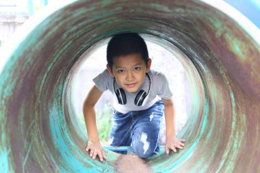Genç bir çocuk kulaklık takarak bir oyun alanı tünelini zevkle keşfediyor. Meraklı doğası ve neşeli ruhu açık havada eğlenirken parlıyor..