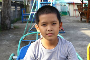 Genç bir çocuk çocuk çocuk parkında düşünceli bir şekilde oturur, çocukluk masumiyetinin ve keşfinin özünü renkli oyun ekipmanlarıyla dolu bir açık hava ortamında yakalar..