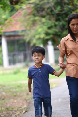 Genç bir çocuk, anne babasıyla el ele, sakin bir açık yolda yürüyor, doğanın güzelliği arasında bir bağlantı anı ve sıcaklık gösteriyor..