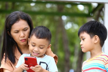 Bir anne ve iki küçük çocuğu ellerinde akıllı bir telefonla dışarıda kaliteli zaman geçiriyorlar. Sevgi ve bağlarını gösteriyorlar..
