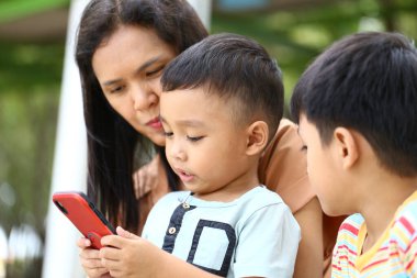 Bir anne ve iki küçük çocuğu açık havada birlikte vakit geçiriyorlar, akıllı bir telefonla meşgul oluyorlar. Sahne, aile sıcaklığını ve bağlantısını gelişigüzel bir ortamda yakalıyor..