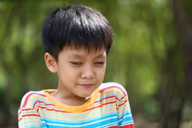 Düşünceli bir ifadeye sahip genç bir çocuk doğada huzurlu bir anın tadını çıkarıyor. Onun renkli çizgili gömleği yemyeşil arka plana karşı duruyor, masumiyet ve merakı yakalıyor..