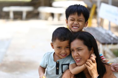 Güneşli bir park ortamında gülümseyen iki çocuğuyla eğlenen bir annenin canlandırdığı yürek ısıtan bir sahne..