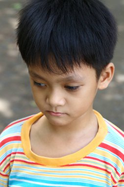 Düşünceli genç bir çocuk renkli çizgili bir gömlekle aşağıya bakıyor. Bu portre, açık hava ortamında bir yansıma anı yakalar..