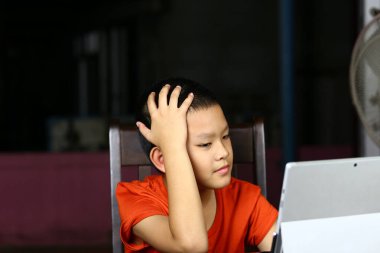 Evde online öğrenmenin zorluklarını vurgulayan genç bir çocuk tableti üzerinde çalışırken hayal kırıklığına uğramış görünüyor. Görüntü, modern eğitim mücadelelerini yansıtıyor.