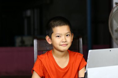 Neşeli bir çocuk tabletle bir masada otururken gülümsüyor, kapalı bir ortamda neşeli ve eğlenceli bir atmosfer sergiliyor, eğitim ve teknoloji temaları için mükemmel..