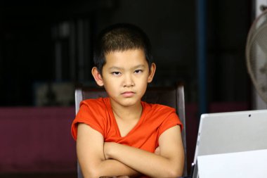 Genç bir çocuk dizüstü bilgisayar kullanırken ciddi bir ifadeyle masada oturuyor. Parlak iç mekan ayarları öğrenme ortamında odaklanma ve kararlılığını gösteriyor.