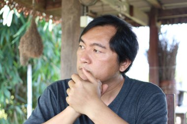 Düşünceli bir adam dışarıda oturur, derin düşüncelere dalmış. Doğal yeşilliklerle çevrili, yansımayı ve iç gözlemlemeyi davet eden sakin bir tavır sergiliyor..