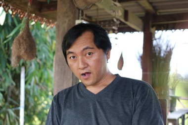 Açık havada, yeşilliklerle çevrili otururken şaşkınlığını ifade eden samimi bir portre. Görüntü, gerçek bir duygu ve yaşam tarzını yakalar..