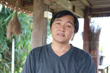 Düşünceli bir adam yeşilliklerle çevrili kırsal bir yerde oturur. Onun sakin ifadesi doğadaki huzur ve sükuneti yansıtıyor..