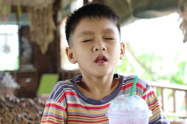 Neşeli bir çocuk güneşli bir kafede oturmuş, ferahlatıcı bir içkinin tadını çıkarıyor. Onun ifadesi çocukluk anlarının masumiyetini ve mutluluğunu yakalar. Eğlenceyi ve eğlenceyi resmetmek için mükemmel.