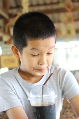 Meraklı bir ifadeye sahip genç bir çocuk kırsal bir kafede soğuk bir içeceğin tadını çıkarıyor. Sahne, yaz temaları için mükemmel olan masumiyet ve neşeyi yakalar..