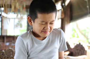 Genç bir çocuk evdeki samimi bir anda rahatsızlığını gösterir. Ciddi ifadesi, doğal ışıkta yakalanan gerçek bir üzüntü hissini yansıtıyor..