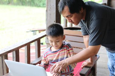 Bir baba, güneşli bir günde oğluna dizüstü bilgisayarda yardım eder. Bu sıcak sahne, açık havada aile bağlarını, öğrenmelerini ve etkileşimlerini sergiliyor..