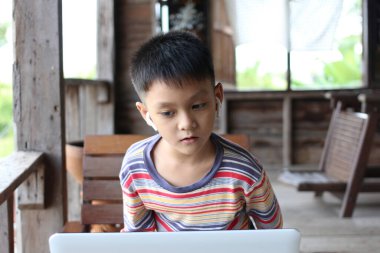 Kırsal alanda dizüstü bilgisayar kullanmaya odaklanmış genç bir çocuk. Kulaklık takıyor ve ekrana merakını ve bağlılığını gösteriyor..