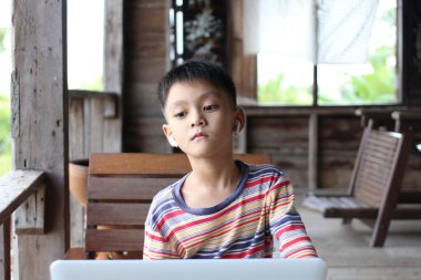 Kulaklık takan genç bir çocuk laptopa odaklanmış, içi ahşap iç kısımlarla çevrili, modern teknolojiyi rahat bir atmosferle harmanlıyor..