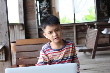 Kır evinde dizüstü bilgisayarla uğraşan genç bir çocuk. Kulaklık takıyor, merakını ve dikkatini gösteriyor. Sıcak ahşap çevreler rahat bir atmosfer yaratıyor..