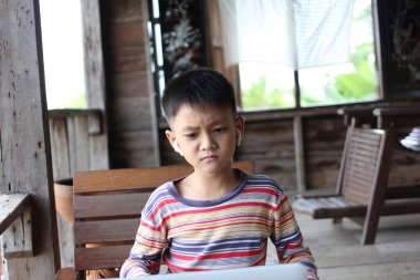 Kulaklık takan genç bir çocuk ahşap bir masada oturuyor, dizüstü bilgisayarına odaklanmış. Kırsal çevre, öğrenmek ve oynamak için uygun gündelik ve yaratıcı bir atmosferi vurguluyor.