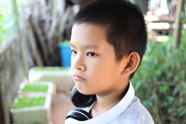 Kulaklık takan düşünceli bir çocuk uzaklara bakıyor. Etrafı yeşilliklerle çevrili, düşüncelerini sakin ve doğal bir ortamda yansıtıyor..