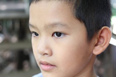 Açık havada düşünceli bir gencin yakın plan portresi, sakin bir ifade ve derin bir bakış sergiliyor, çocukluktaki masumiyet ve tefekküre vurgu yapıyor..