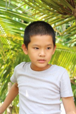 Düşünceli genç bir çocuk, gür tropikal yaprakların arasında düşünceli bir şekilde, dinginlik ve masumiyet anını canlı bir doğal ortamda yakalıyor..